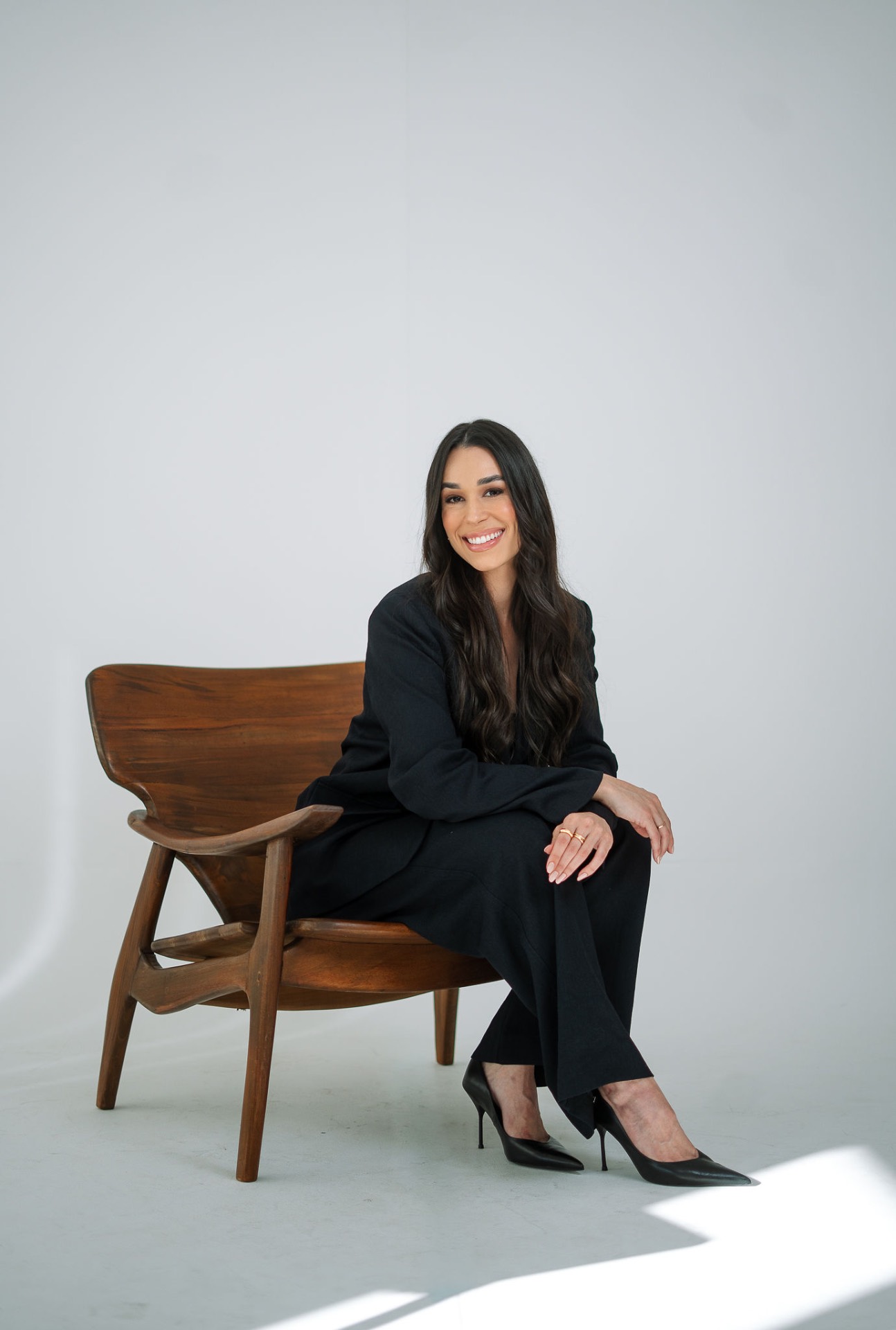 Heloíse Leite sentada em uma poltrona de madeira